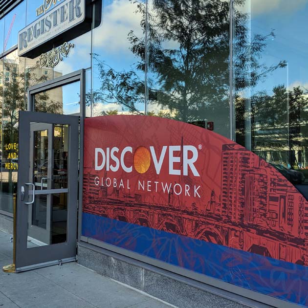 An image of the exterior of the building with adhesive window graphics cut on a curve branded with the Discover Global Network logo and a graphic of the Boston skyline